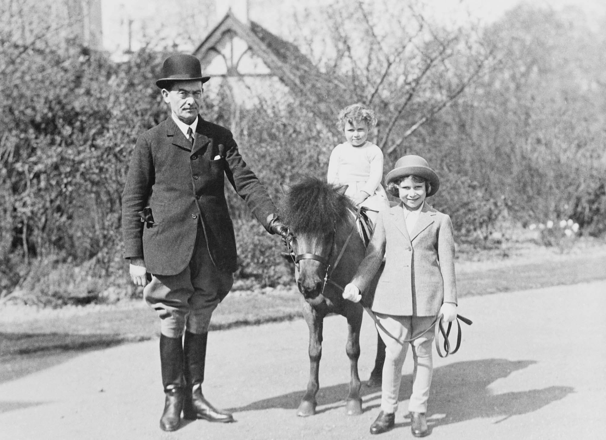 Four-year-old Elizabeth, atop Peggy, with her sister Princess Margaret and an unidentified groom, about 1933.