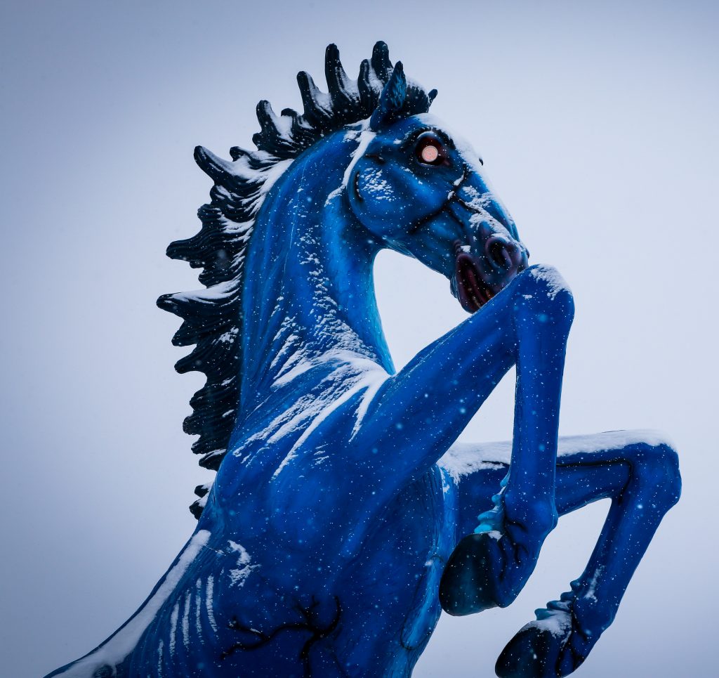 Denver International Airport's Blue Mustang statue rears up amid snowfall, it's neon red eyes piercing.