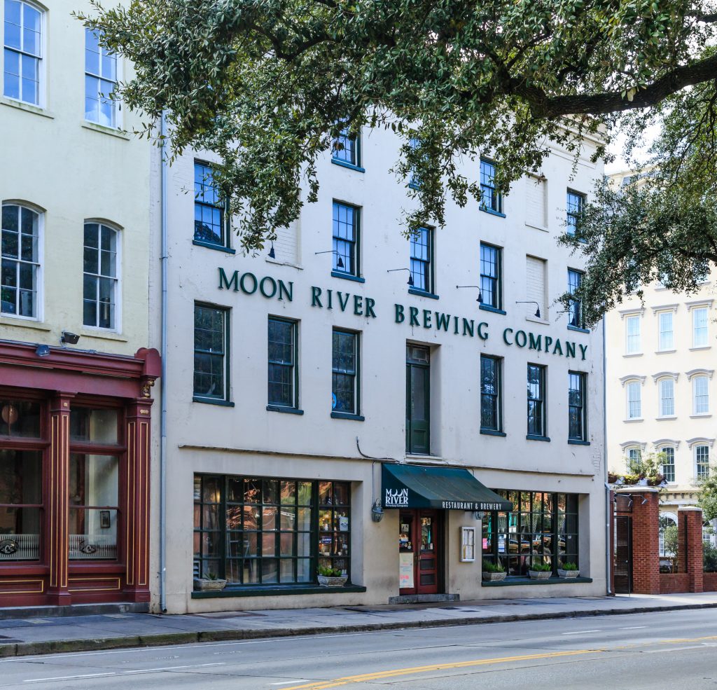 The beige exterior of the Moon River Brewing company in Savannah bears the brewery's name in green along with a green awning.