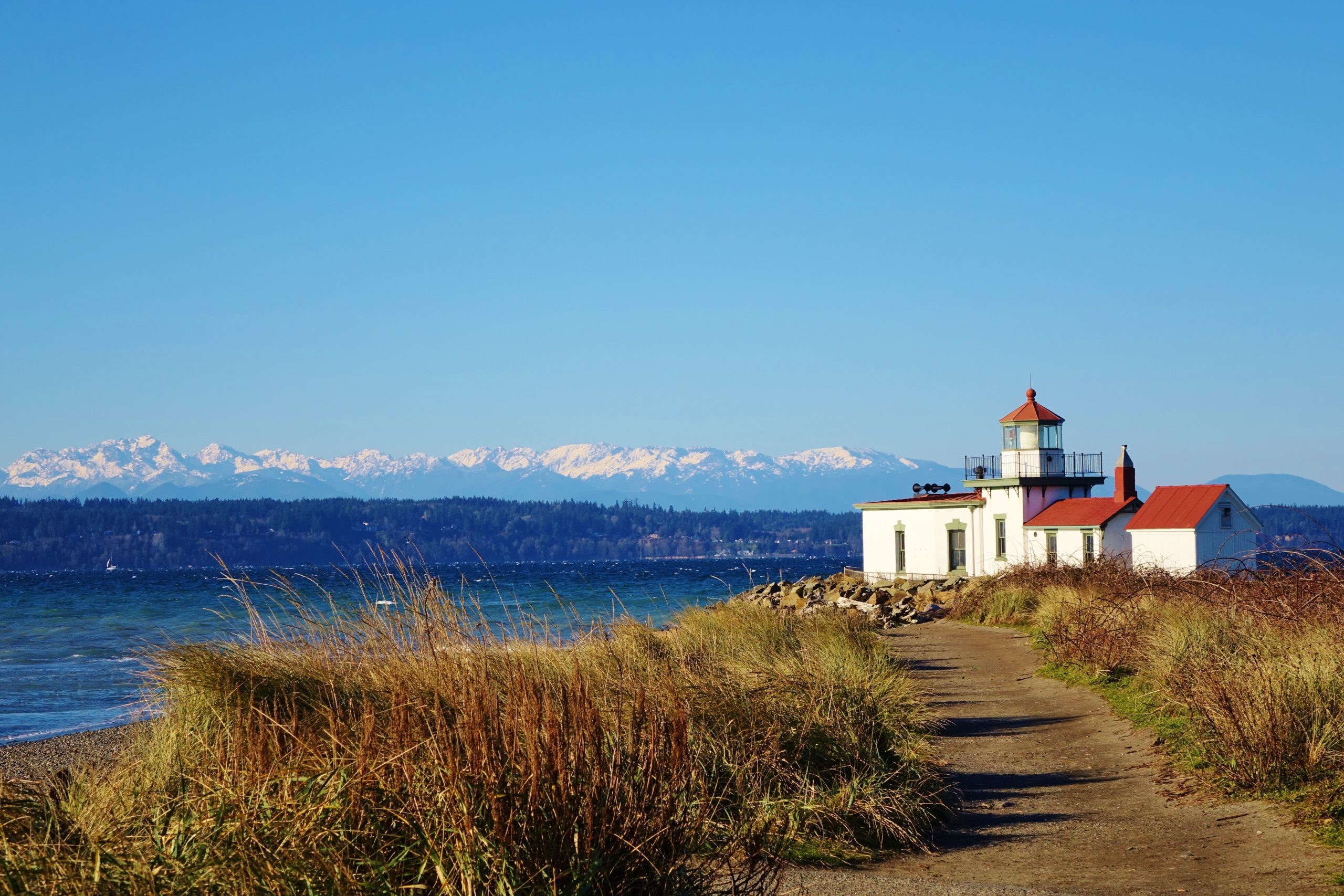 The West Point Lighthouse sits on the cliffs at Discovery Park in Seattle with the Olympic Mountains in the background.