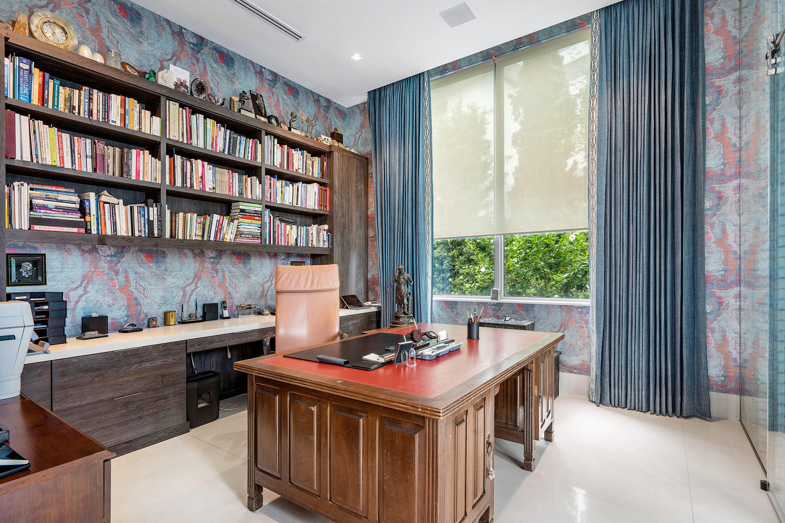 An office at 7170 Ayrshire Lane in Boca Raton sports vibrant wallpaper patterns of blue, red, and purple with built-in bookshelves and a dark brown wooden desk.