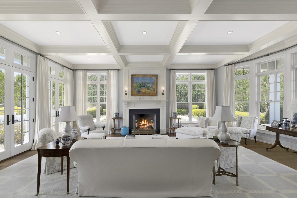 Coffered ceilings sit above the fireplace and white furniture of the living room at 233 Gin Lane.