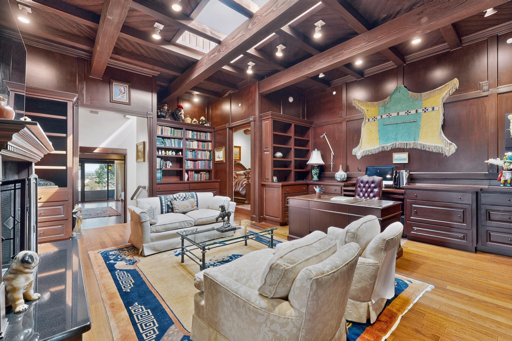 1308 Thunder Ridge A wood-paneled home office with exposed ceiling beams, a desk with a leather chair, a sofa, and two armchairs arranged on a patterned rug.