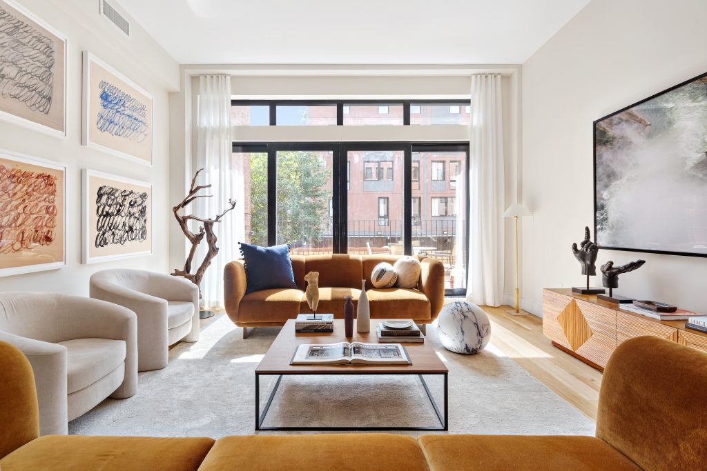 A living room in 436 Clinton Avenue with ochre-colored couches, hand statues, a tree sculpture, and modern art on the walls.