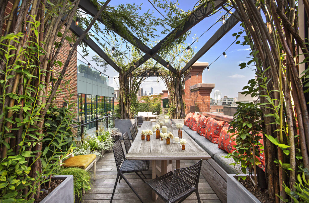 Clear blue skies and the Lower Manhattan skyline is visible from under a willow pergola on a penthouse terrace.