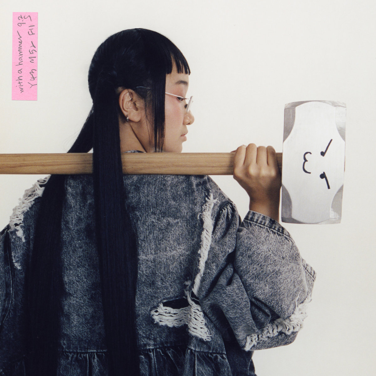 Yaeji holds a sledgehammer with a smirking face drawn on it. She looks cool as hell.