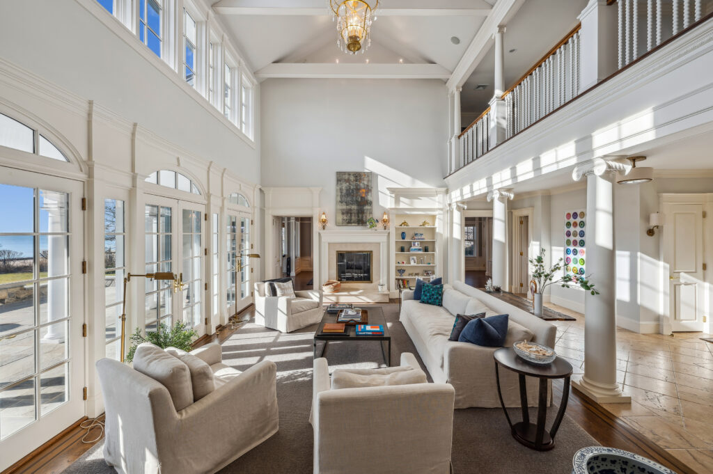 Sunlight illuminates a living room with Ionic columns, a balcony, and a fireplace.