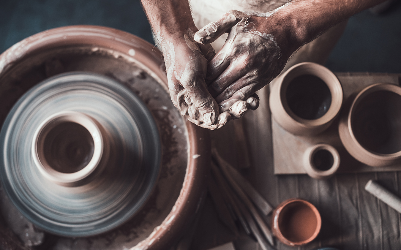 A potter at work molding their pottery on a pottery wheel.