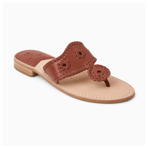 A brown leather slip-on sandal with intricate stitching and cutout floral designs on the strap, a low wooden heel, and a beige sole—perfect for flipping through cookbooks in style.