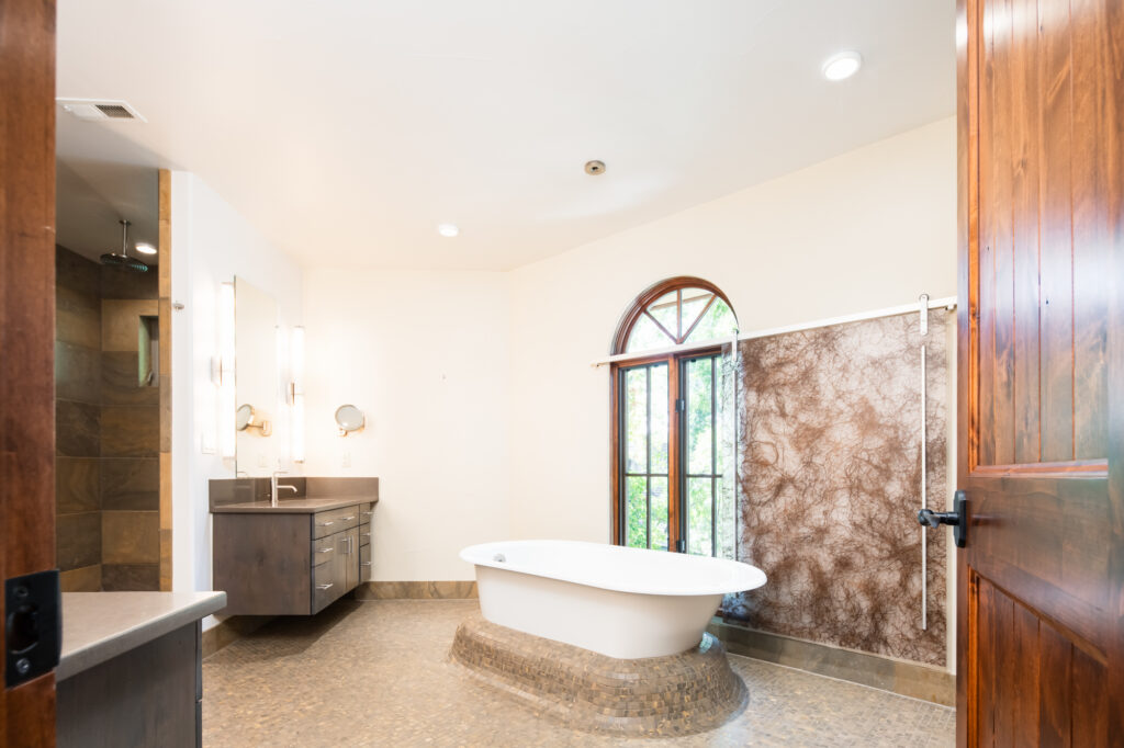 The earth tone tiles of this primary bathroom form a hill for a cast-iron bathtub to rest atop.