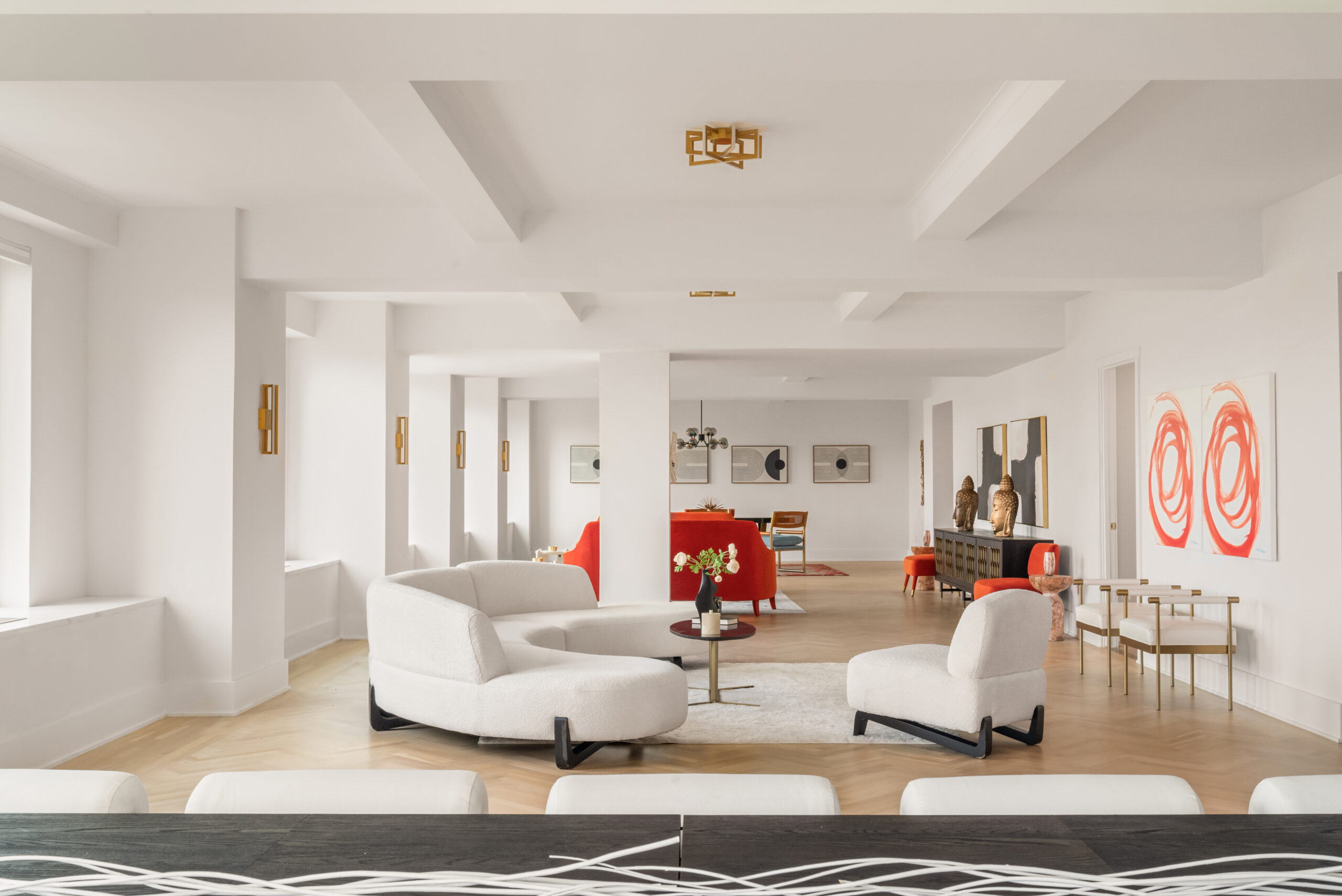 A spacious great room with white furniture, red accents, abstract art, and large windows overlooking Central Park.