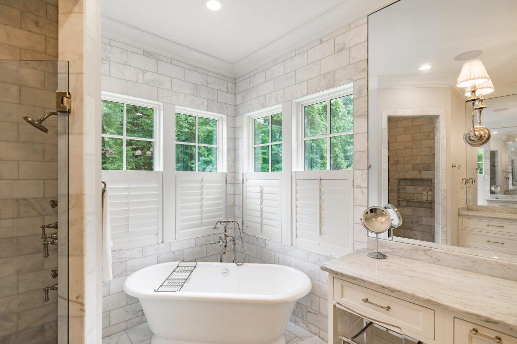 A classic soaking bathtub inside of a modern marble primary bathroom.