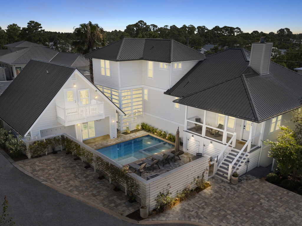 Modern residential property with two white buildings connected by a courtyard featuring a rectangular swimming pool, outdoor furniture, and twilight lighting creating a warm ambiance.