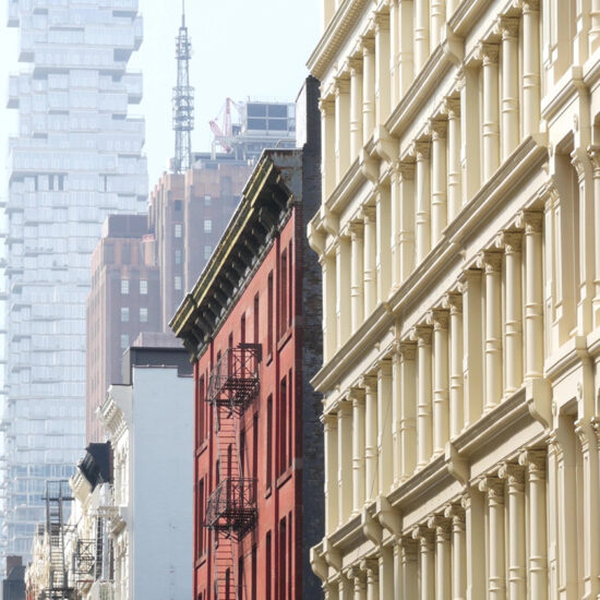 A city street with a mix of modern and historic buildings, including a unique stacked building in the background.