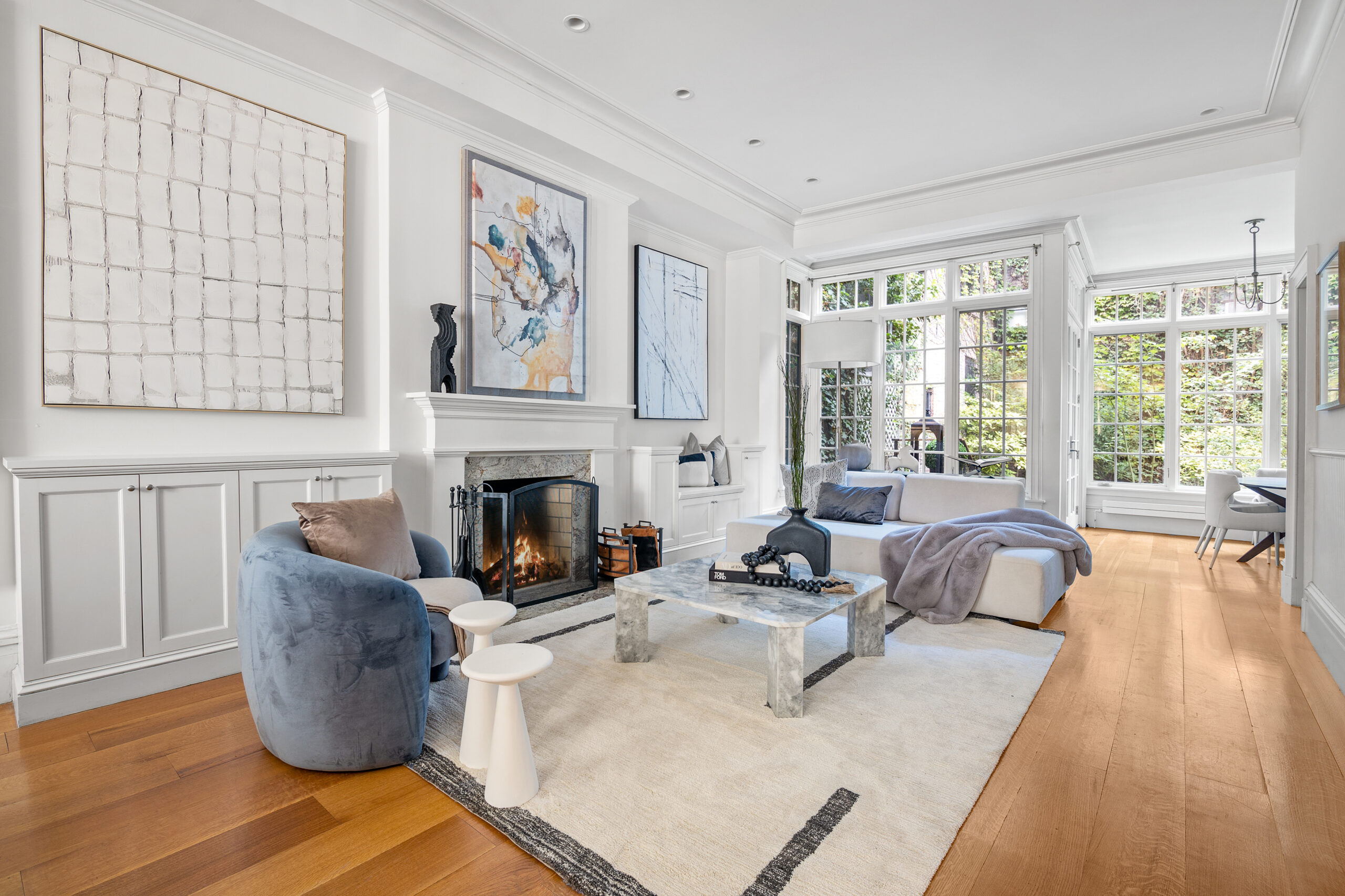 A bright, modern living room with large windows, wood floors, a marble coffee table, a gray armchair, and a white sofa—perfect for hosting your A-list: September 2025 gatherings by the fireplace and built-in white cabinets.