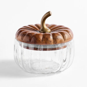 A clear glass jar shaped like a pumpkin with a carved wooden lid and a curved metal stem on top, perfect for storing treats or small cookbooks, set against a white background.
