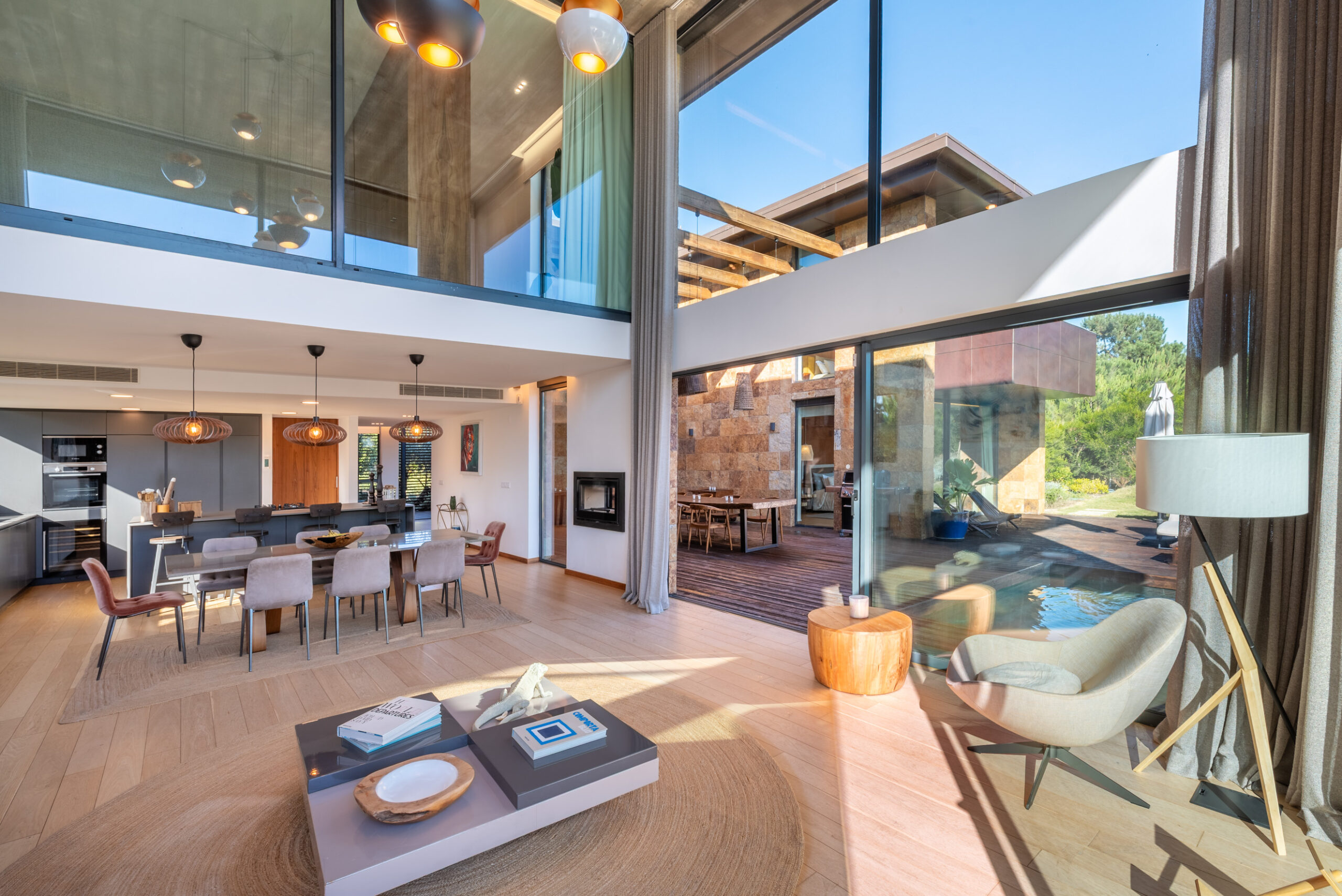 A spacious, modern open-plan living and dining area with floor-to-ceiling windows, wooden floors, stylish furniture, and views of a patio and garden—a perfect retreat for your A-list: December 2025 gatherings on a sunny day.