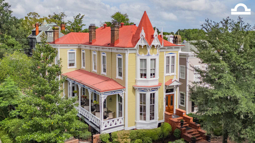 A large, two-story Victorian house with a red roof, yellow siding, white trim, ornate gables, and a wraparound porch, surrounded by trees and greenery on a sunny day—perfect for reflecting on astrological houses during Sagittarius season.