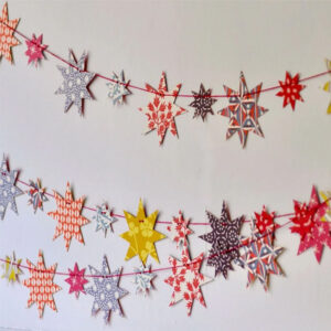 Colorful paper star garlands with various patterns are hanging against a white wall, creating a festive and cheerful decoration—perfect for brightening up spaces near your cookbooks.