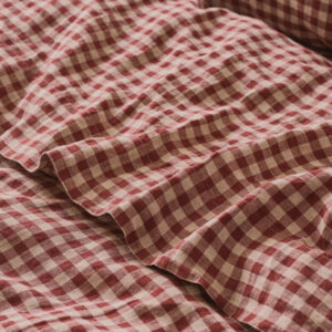 A close-up of crumpled fabric with a red and white gingham checkered pattern, reminiscent of traditional tablecloths often seen in classic cookbooks, showing soft folds and texture.