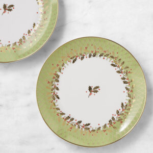 Two decorative plates with green and gold edges, featuring a holly and berry pattern, sit on a white marble surface—perfect for displaying holiday treats or pairing with festive cookbooks.