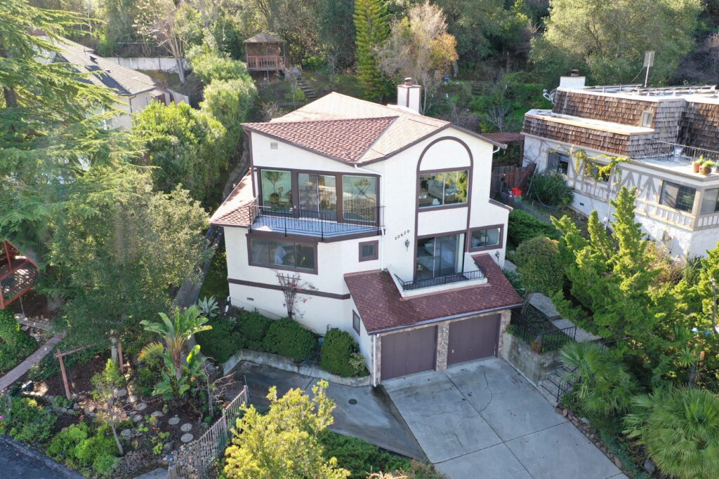 A two-story white house with a red tile roof, large windows, and a landscaped yard surrounded by trees. Perfect for gatherings during Aquarius season, the driveway leads to a two-car garage, with neighboring houses on each side.