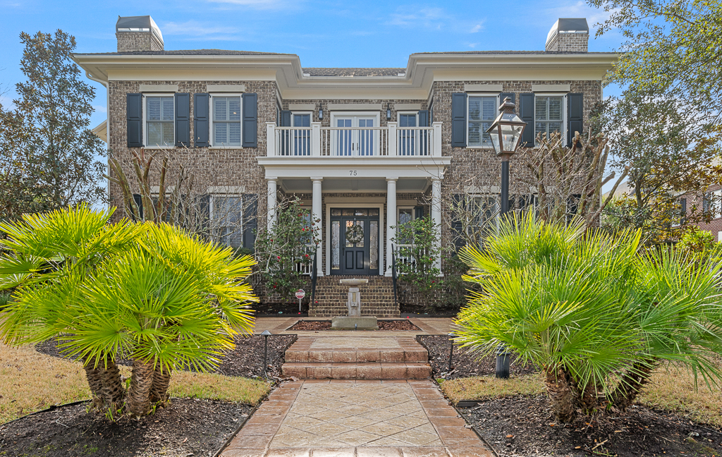 A two-story brick house with white trim, black shutters, and a double front door. Palm plants and manicured landscaping line the walkway, offering serene vibes perfect for reflecting on astrological houses during Pisces season.