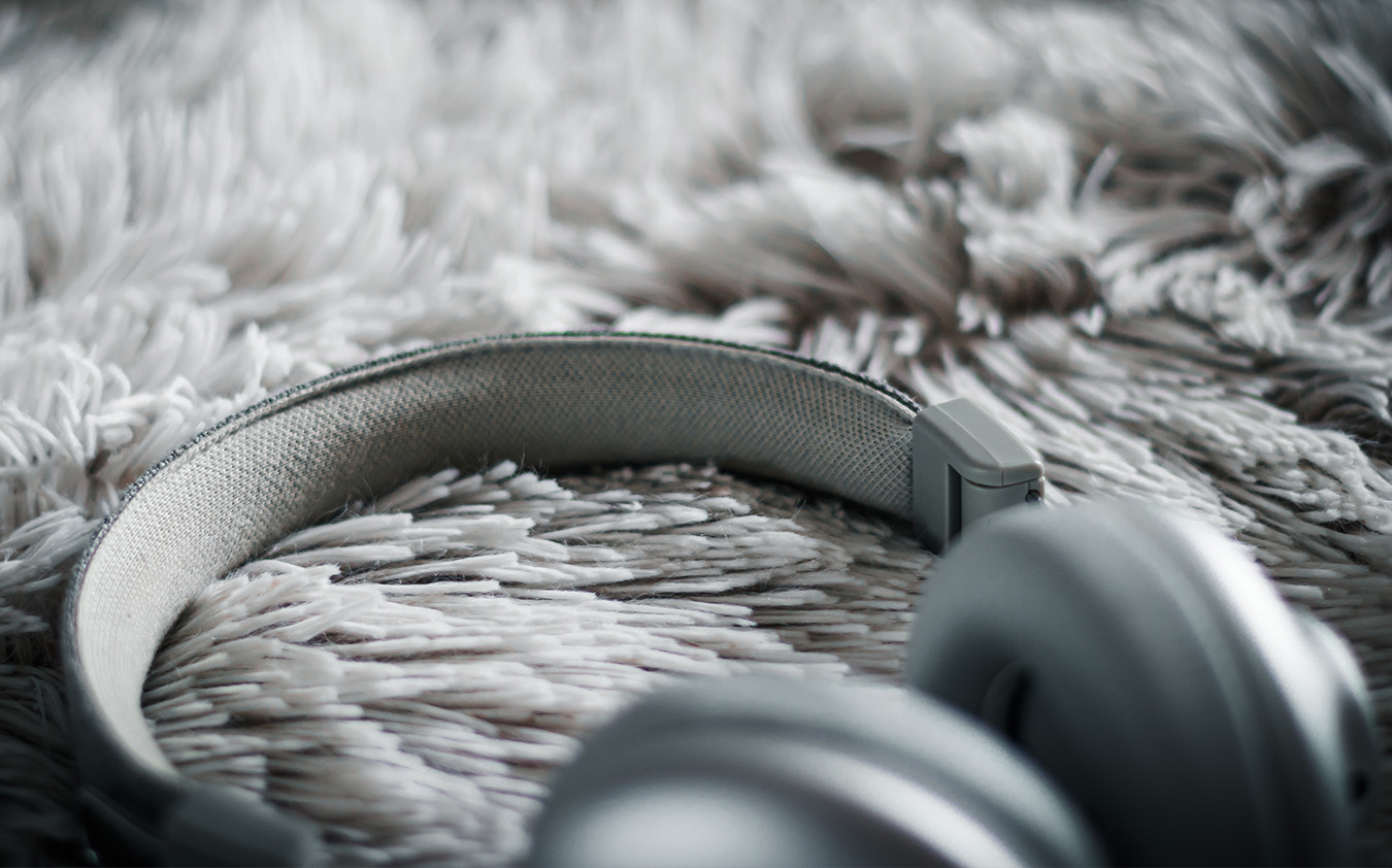 A close-up of gray over-ear headphones resting on a soft, fluffy, light-colored rug—perfect for relaxing after a day of holiday decorating, with the headphone band and part of the ear cups in focus.