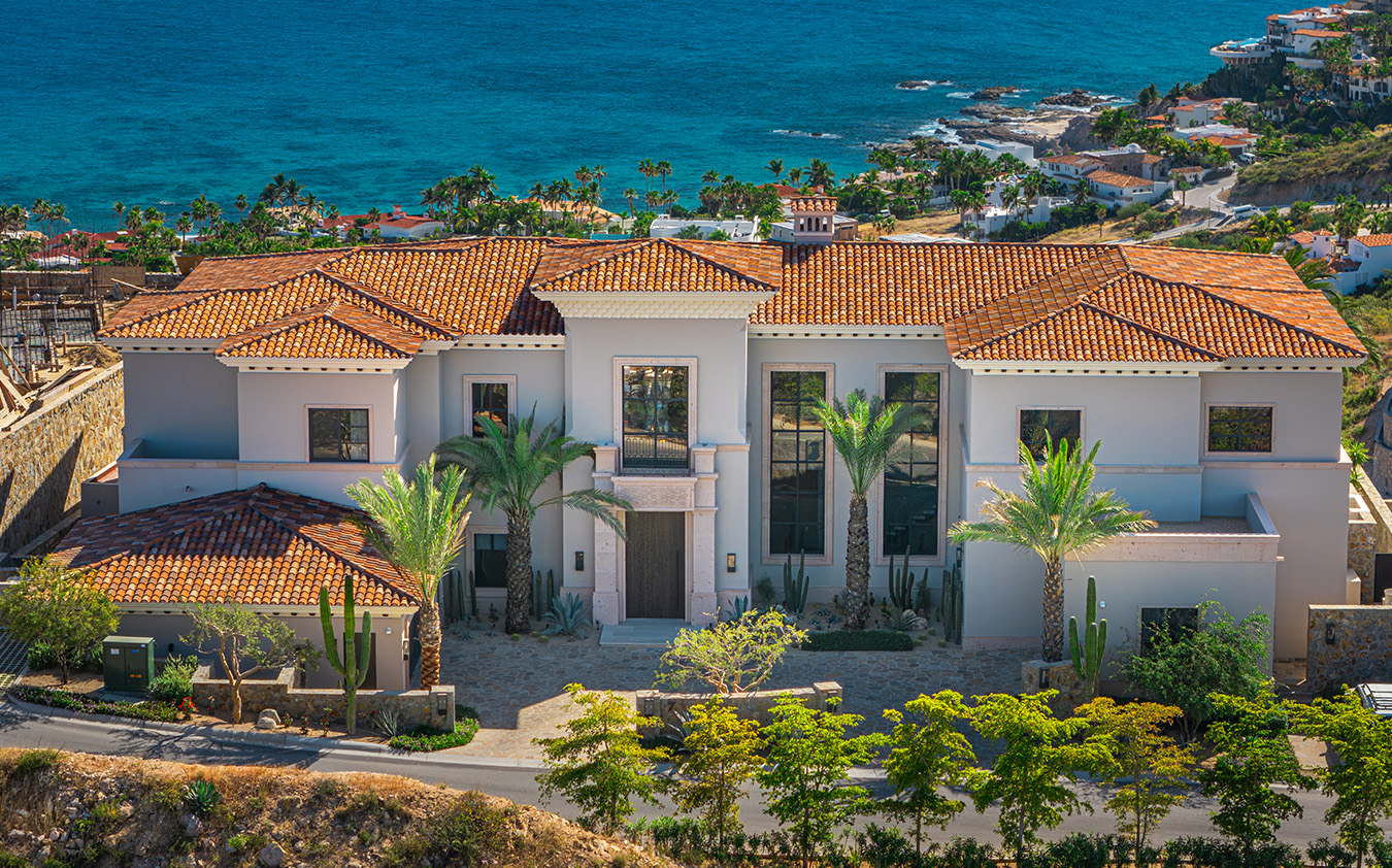 A large, modern Mediterranean-style villa with terracotta roof tiles and palm trees stands overlooking the ocean, offering stunning views of coastal homes—a true A-list retreat for March 2026.