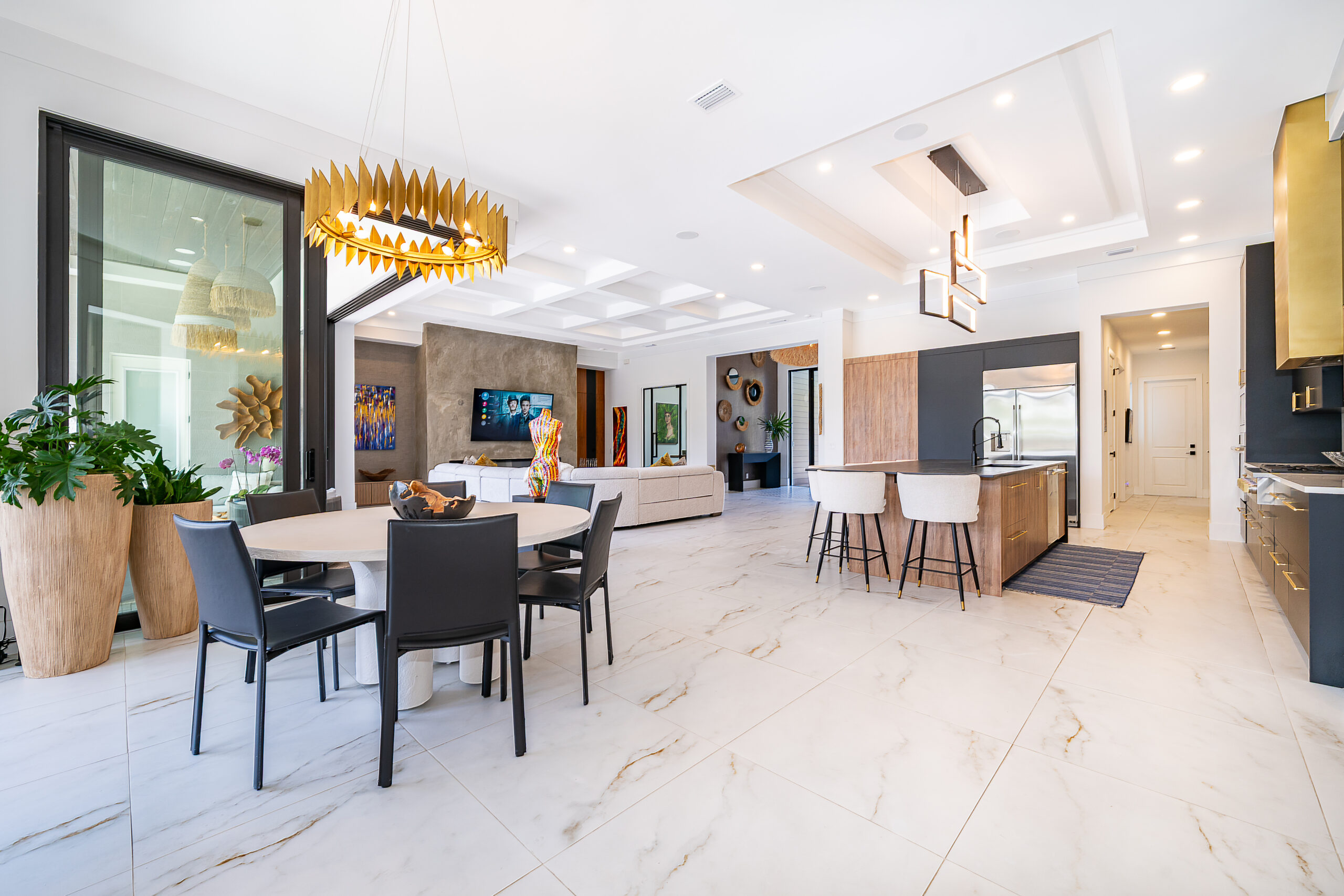 Modern open-concept kitchen, dining, and living area with marble floors, contemporary furniture, gold light fixtures, potted plants, and large windows letting in natural light—a-list style for May 2026.