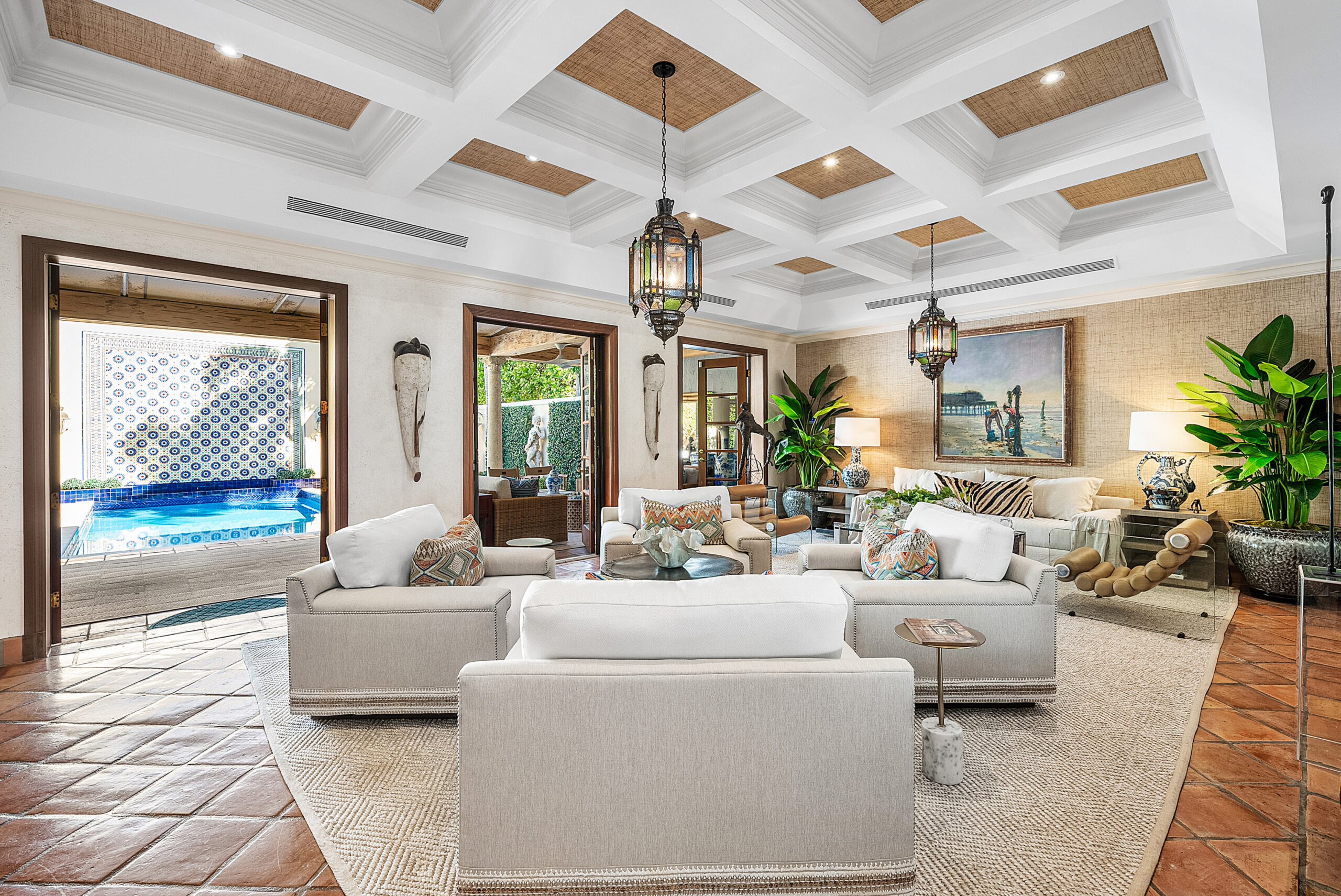 Spacious, elegant living room with white couches, patterned pillows, large plants, and hanging lantern lights. Open doors lead to a small pool outside. Perfect for entertaining guests or hosting an a-list: april 2026 gathering.
