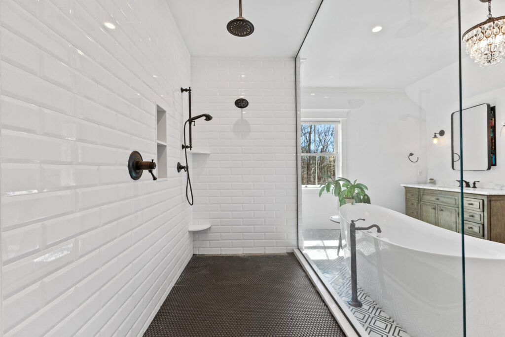 Modern bathroom with a spacious walk-in shower featuring white subway tiles, matte black fixtures, and a rainfall showerhead—perfect for enjoying your own april showers. A freestanding bathtub and large window are visible in the background.
