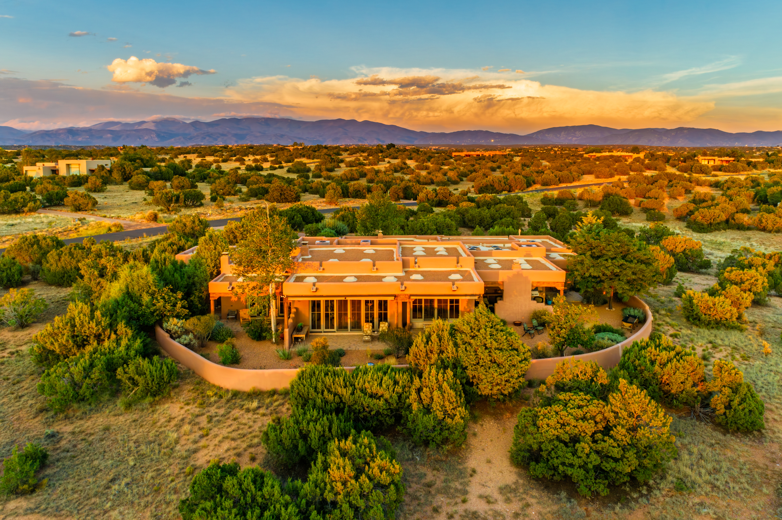 Aerial view of a Southwest-style adobe house, an a-list: May 2026 architectural gem, surrounded by desert vegetation and mountains beneath a colorful sunset sky.