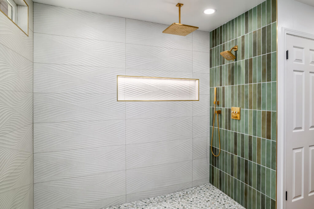 Modern shower with textured white wave-patterned tiles, green vertical tiles, and gold rainfall showerhead evokes the fresh feeling of April showers. Built-in rectangular niche with gold trim is set in the wavy wall for elegant storage.