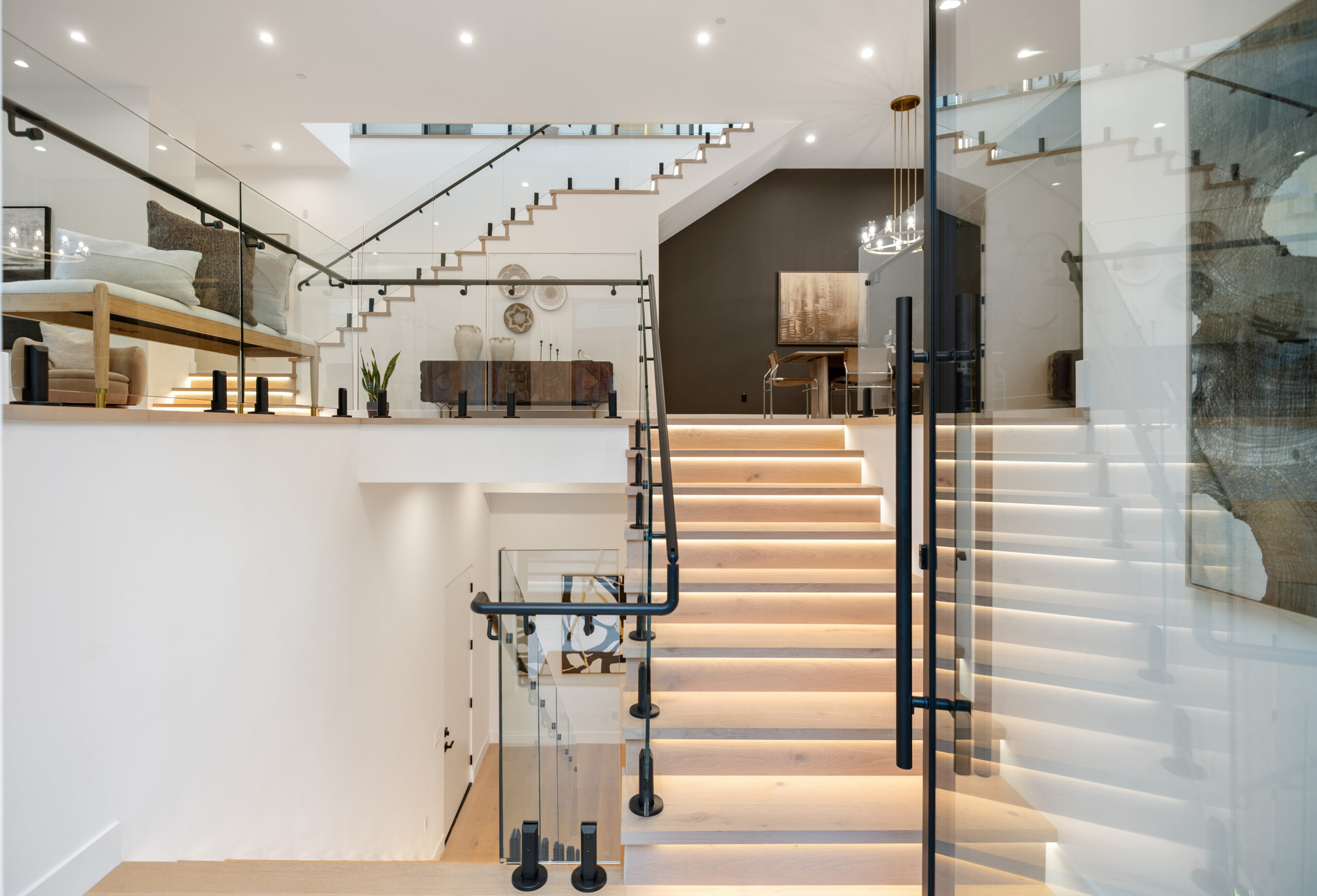 A modern, open-concept home interior with light wood stairs, glass railings, and black accents—designed to impress any a-list guest: june 2026. The bright space features minimalistic decor, large artwork, and contemporary lighting fixtures.