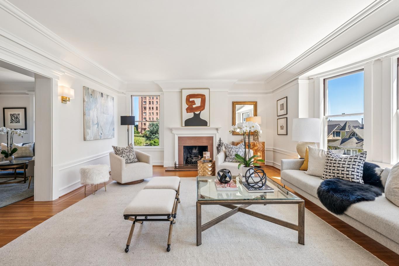 Elegant living room with white walls, neutral furniture, modern art above a fireplace, large windows letting in natural light, and contemporary decor on a glass coffee table—perfect for entertaining guests or relaxing in A-list style: August 2026.