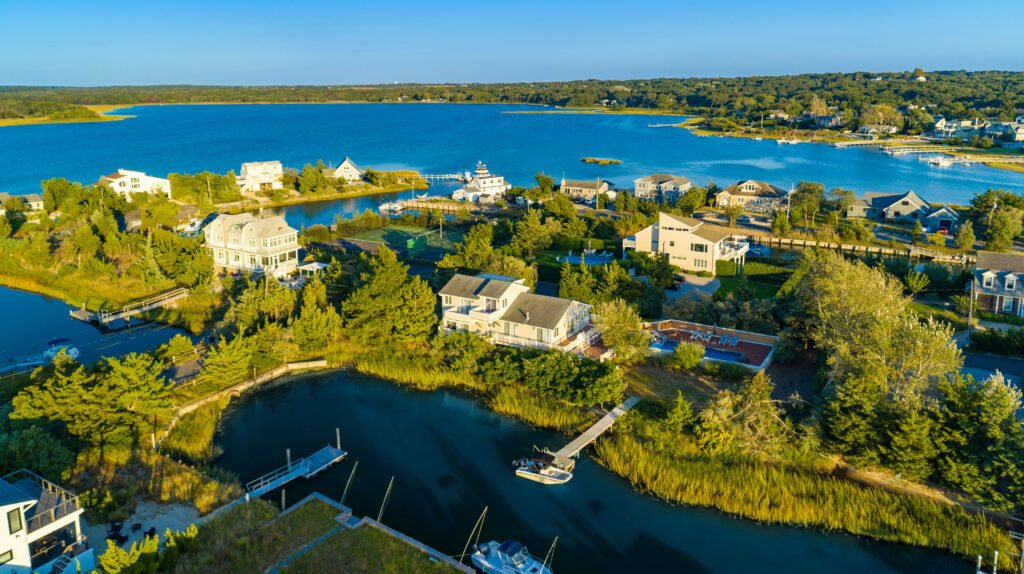 Aerial view of waterfront homes with docks along a calm river, opening to a large blue lake surrounded by green trees and residential houses under a clear blue sky—capturing the vibrant energy and bright days of leo season.