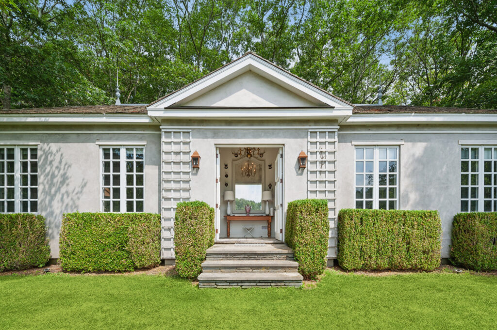 Elegant guest house exterior featuring a symmetrical façade, manicured boxwood hedges, classic divided-light windows, and a welcoming entryway, showcasing luxury estate architecture and refined garden design.