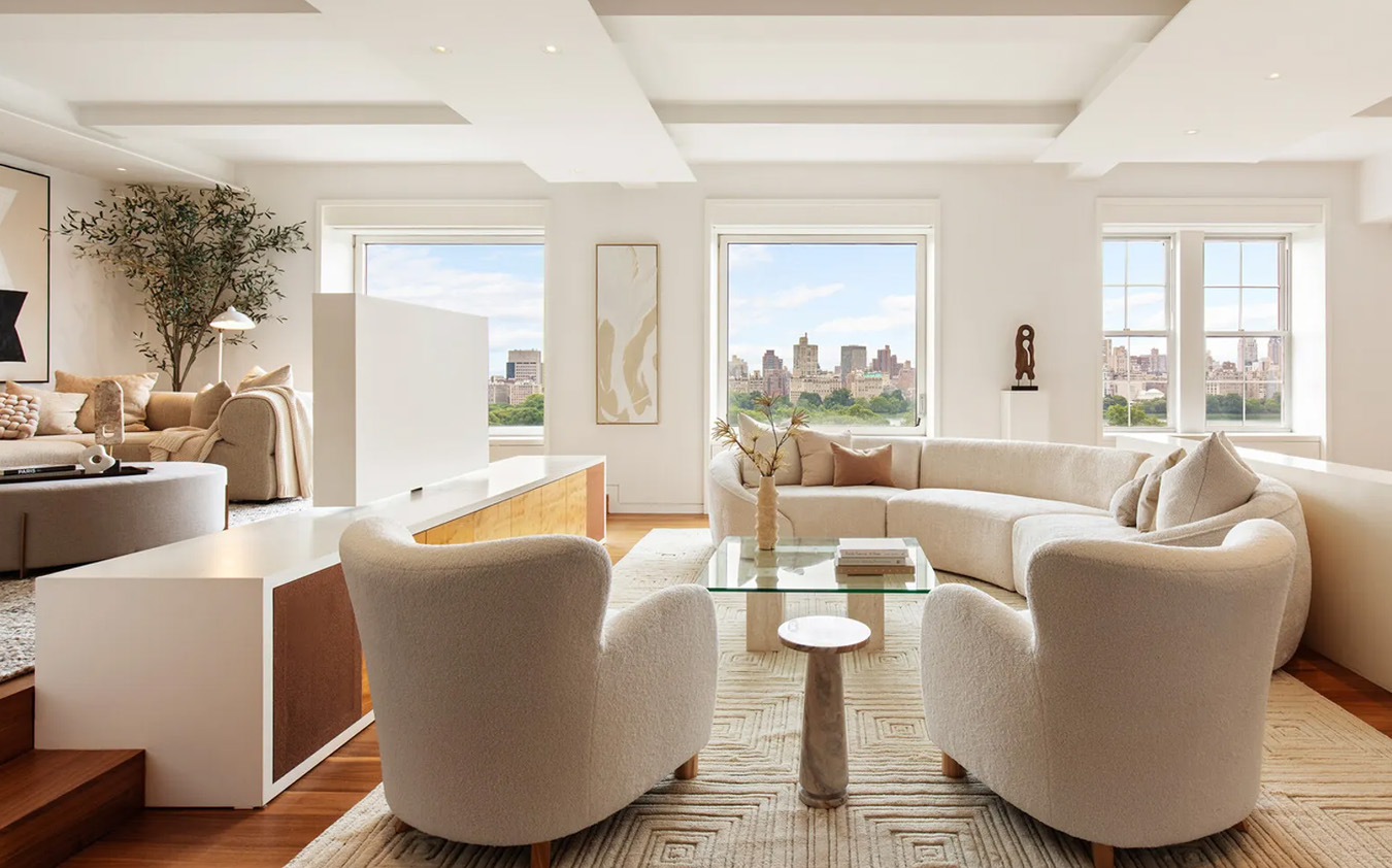 A bright, modern living room with curved white sofas, two armchairs, a glass coffee table, large windows, city views, neutral tones, and minimalist decor.