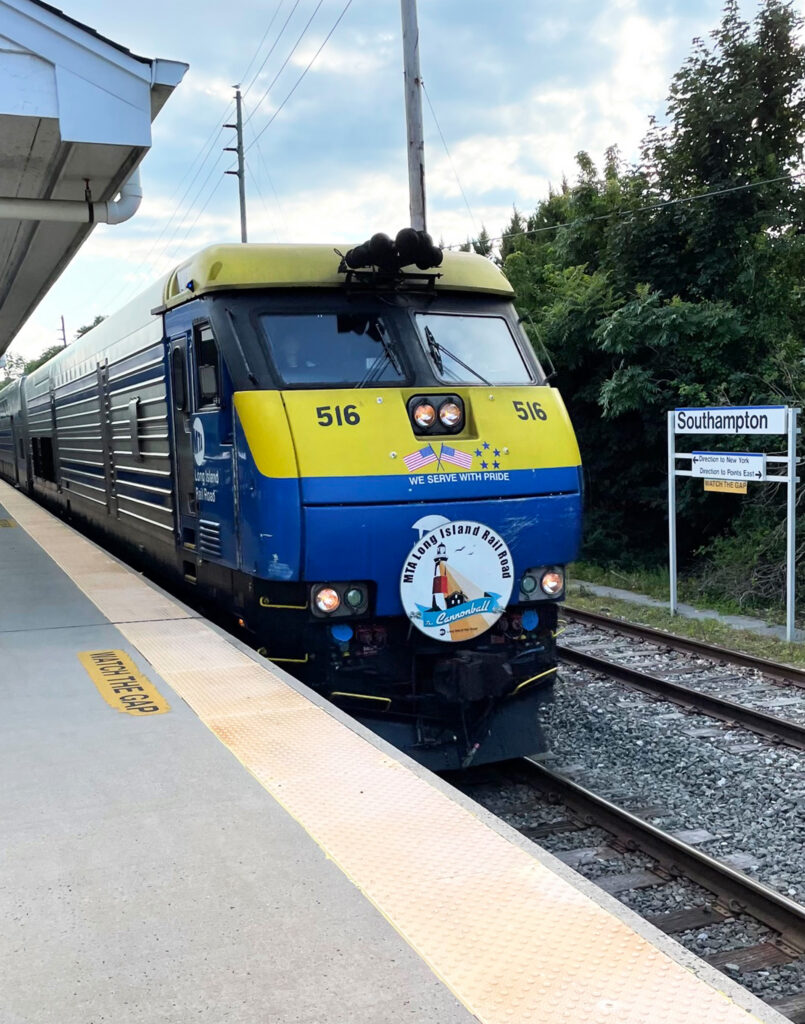 A blue and yellow train labeled 516 stops at a platform next to a sign reading Southampton. The front of the train displays a map logo and the words Long Island Rail Road. Trees are visible in the background.