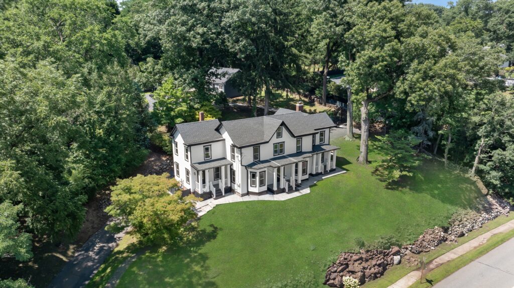 Aerial view of a large white two-story house with a wraparound porch, surrounded by green grass, trees, and a stone-lined yard on a sunny day—an inviting scene that perfectly captures the harmonious energy of Libra season.