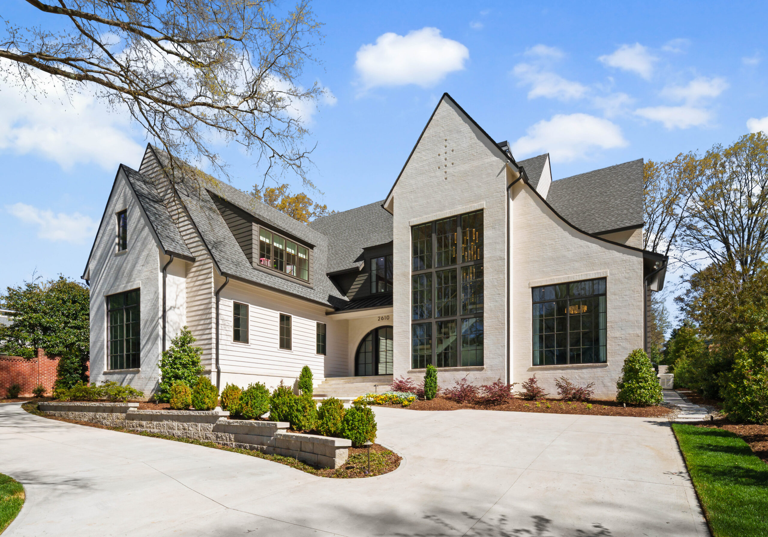 Modern two-story house with white brick exterior, large windows, and dark roof, surrounded by landscaped greenery and a wide concrete driveway under a bright blue sky—a stunning example of contemporary living that could easily belong on any A-list for September 2026.