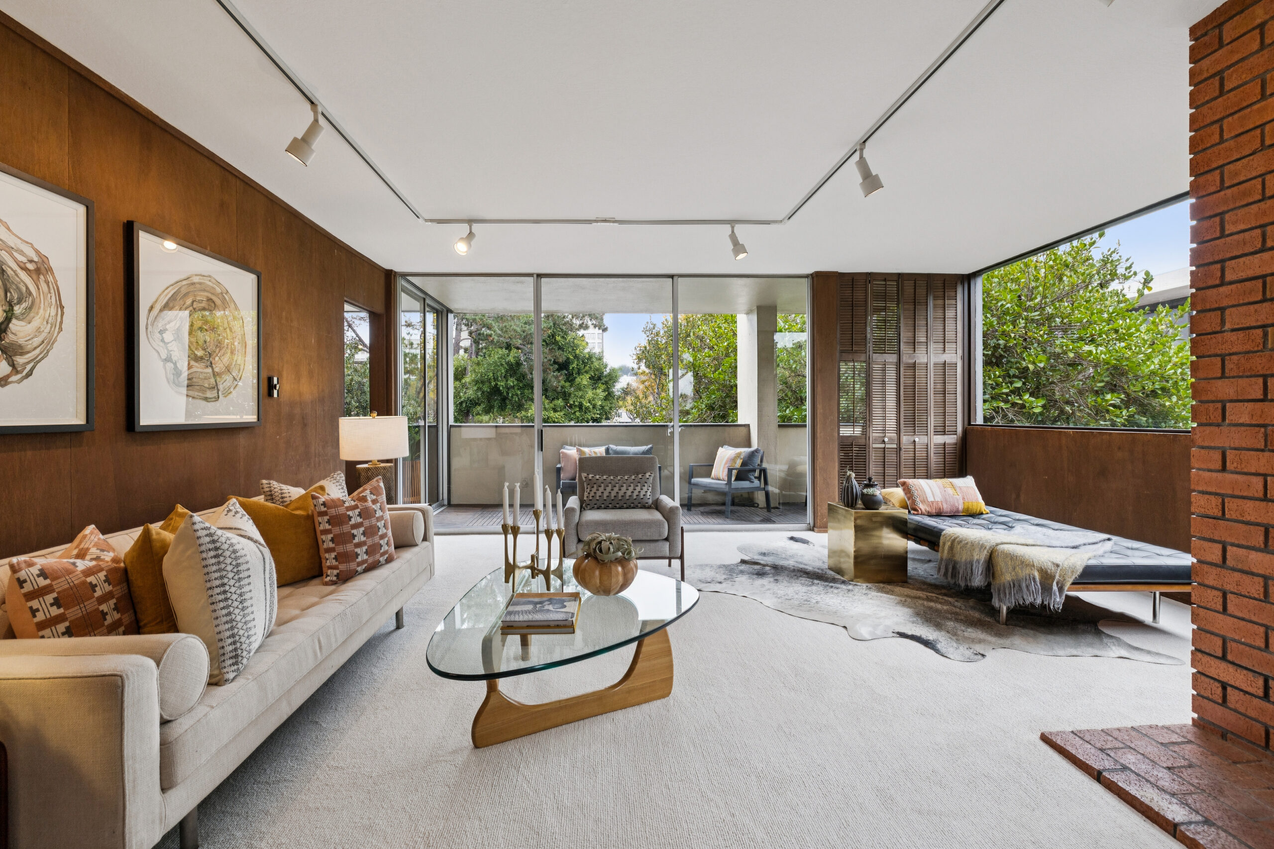 A living room with a beige sofa, glass-topped coffee table, and lounge chair, with floor-to-ceiling windows leading to a balcony as seen in November 2026.