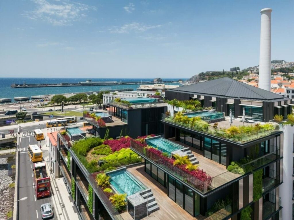 Savoy Residence - Insular Funchal, 9000-054 Funchal, 9000-054 Aerial view of multi-story guest houses featuring tiered rooftop terraces with private swimming pools and gardens, overlooking a coastal city and harbor.