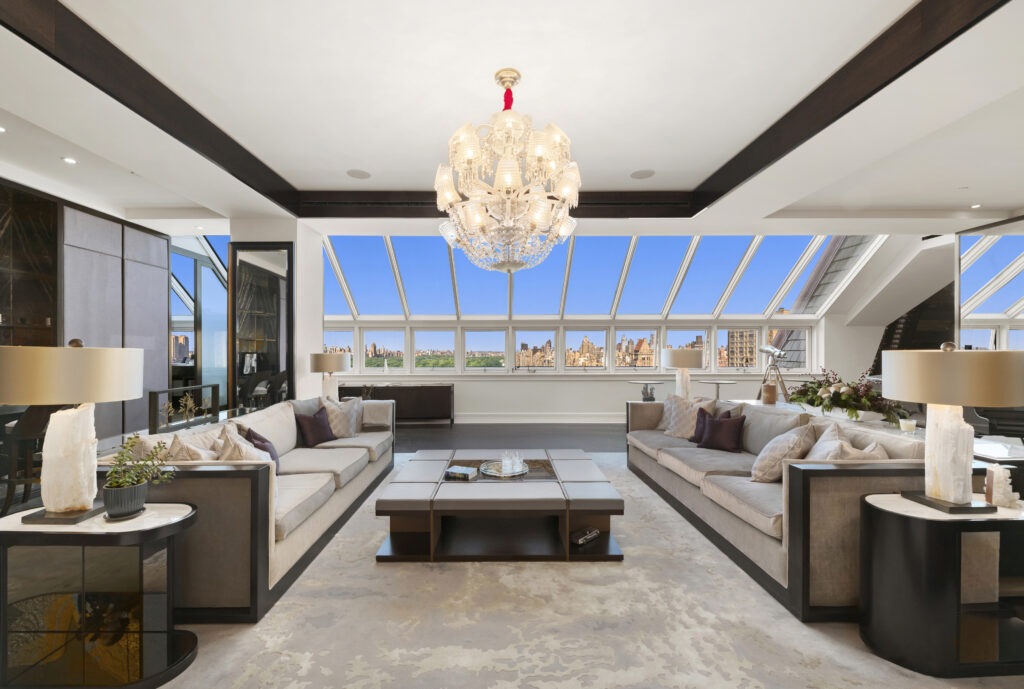 1 cps-10 Living room in a hotel-branded property featuring two facing sofas, a large central ottoman, and a glass-paneled ceiling looking out over a city skyline.