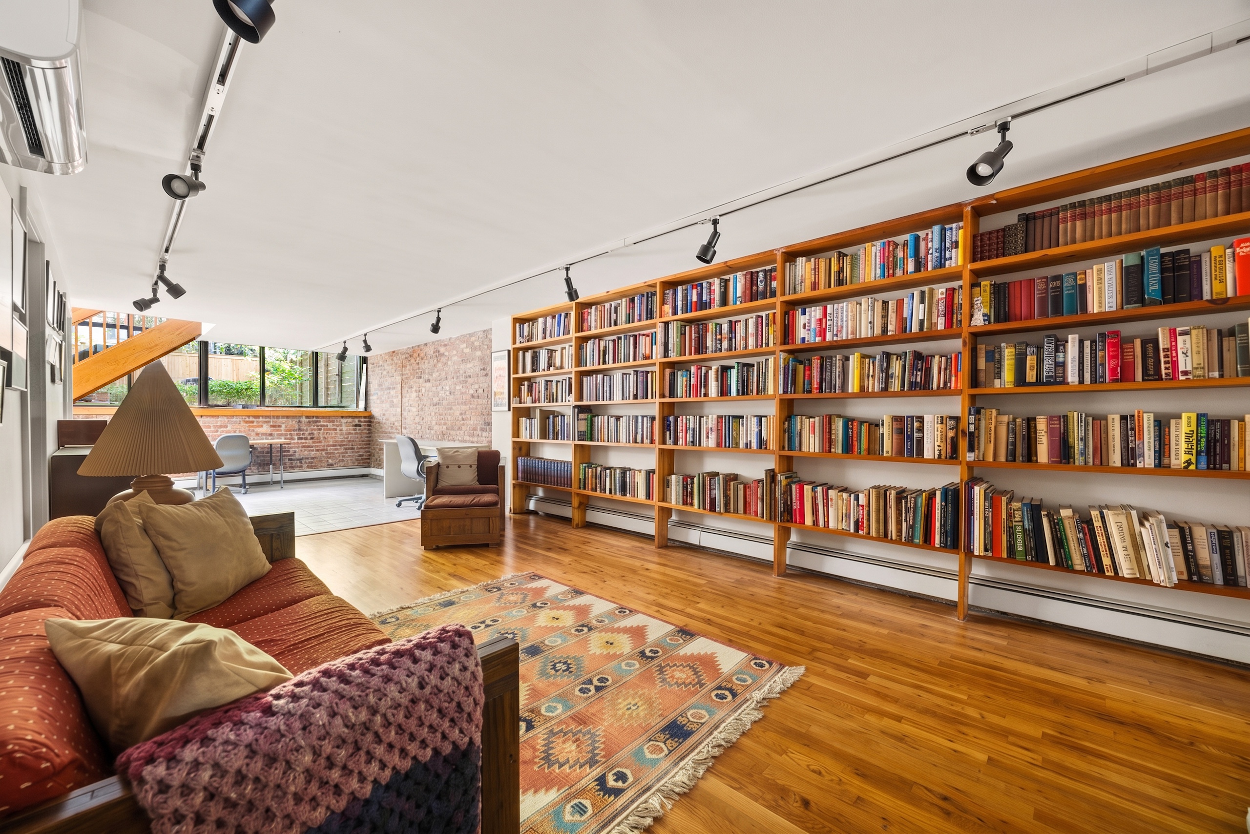 141 St Felix St A living room home office featuring a wall of floor-to-ceiling wooden library shelves filled with books, a sofa with a textured throw blanket, and a patterned area rug on a hardwood floor.
