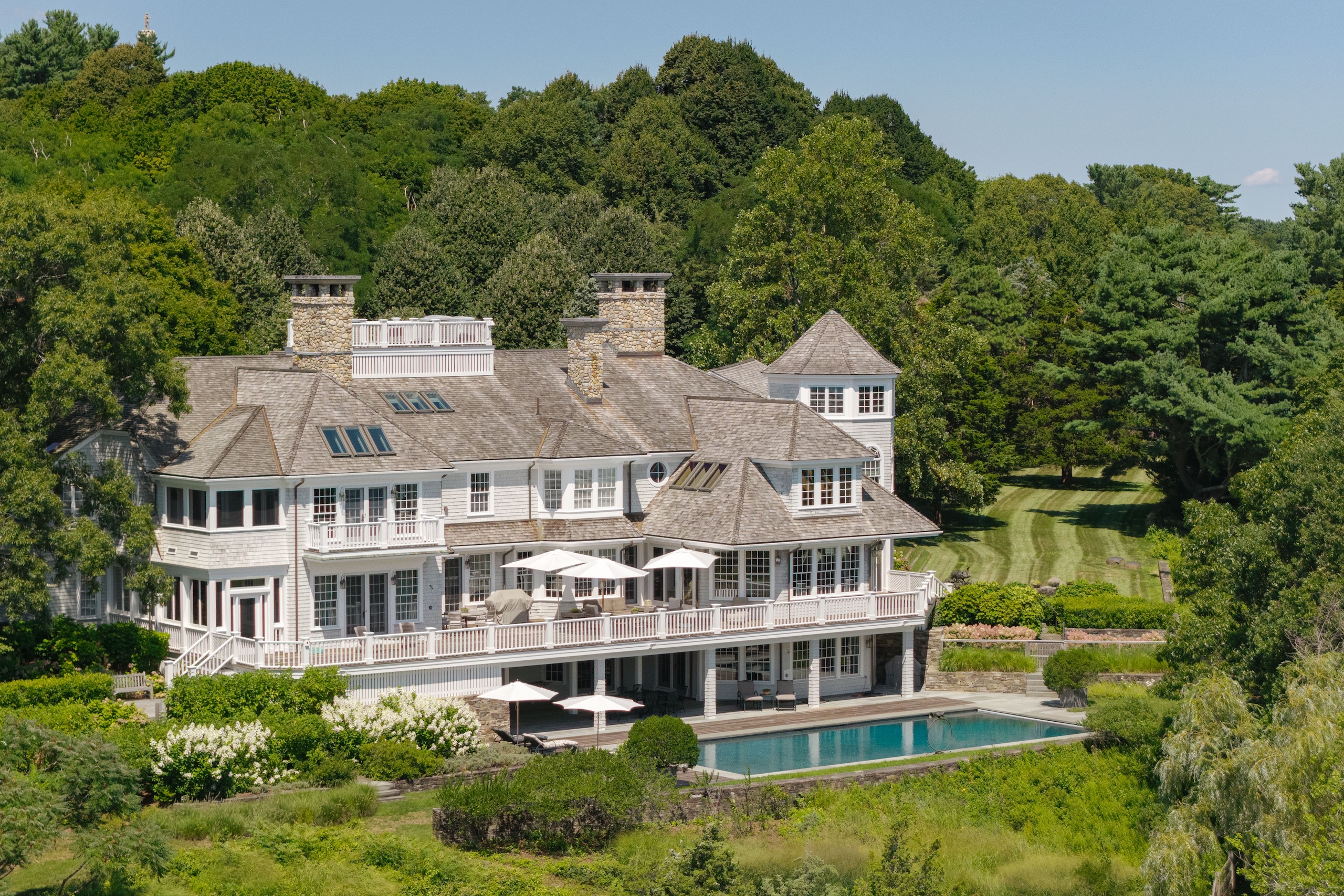 A large, multi-story shingled house with a gray roof, wide decks, and a swimming pool, situated in a wooded landscape featured in our November 2026 A-list.
