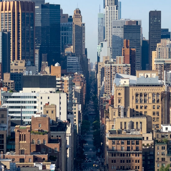 A high-angle view looking down a narrow New York City street canyon between densely packed Manhattan condo skyscrapers.