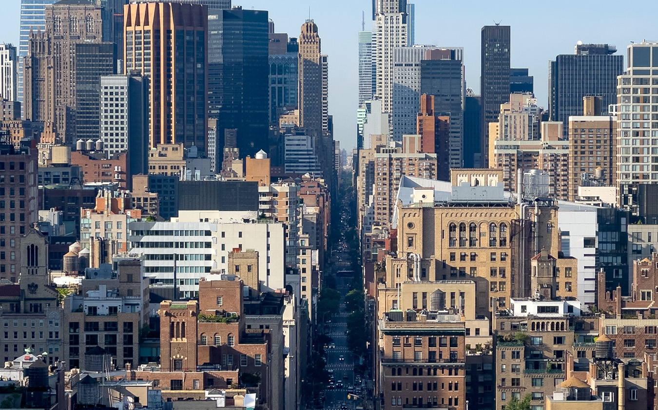 A high-angle view looking down a narrow New York City street canyon between densely packed Manhattan condo skyscrapers.