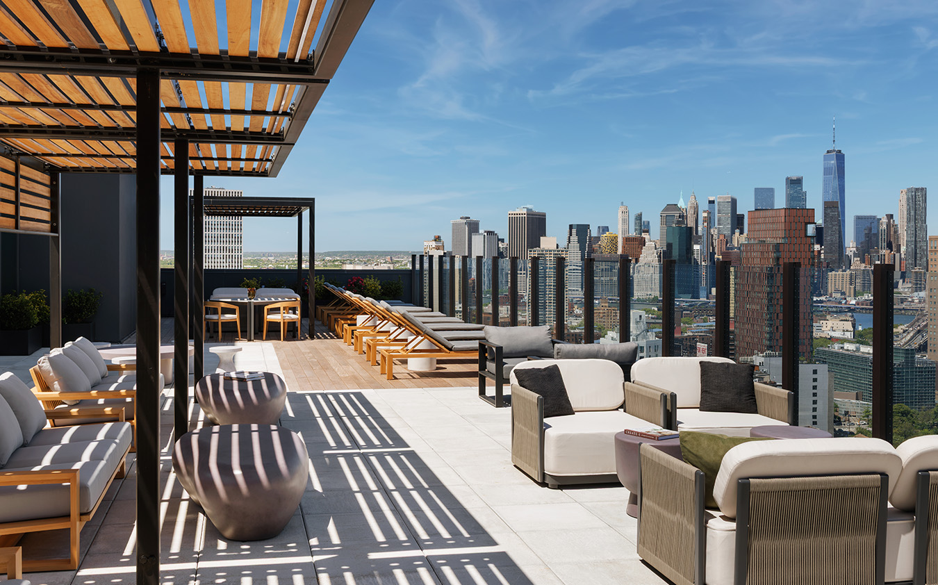 A rooftop terrace featuring multiple seating areas with sofas and lounge chairs, overlooking a city skyline.